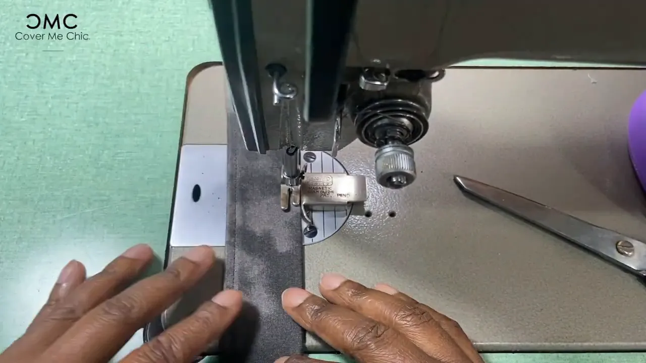 Close-up of a sewing machine stitching a folded knit belt edge guided by hands.